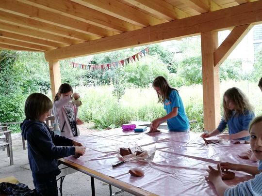 Schülerinnen und Schüler arbeiten im Naturgarten geschützt unter dem Dach des Freiluftklassenzimmers zum BNE-Thema "Leben an Land"
