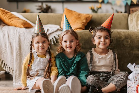 Drei Kinder sitzen nebeneinander und tragen Partyhüte.