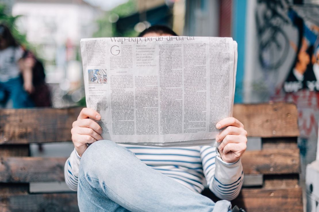 Zeitung lesender Mann, auf einer Bank sitzend