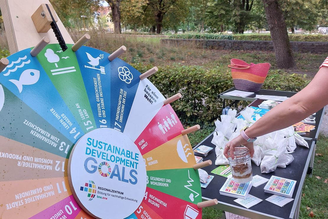 Das Foto zeigt ein SDG-Glücksrad, welches neben einem BNE-Aktionsstand steht 