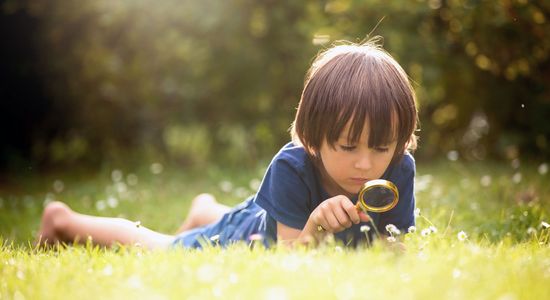 Kind betrachtet im Gras liegend den Boden mit einer Lupe
