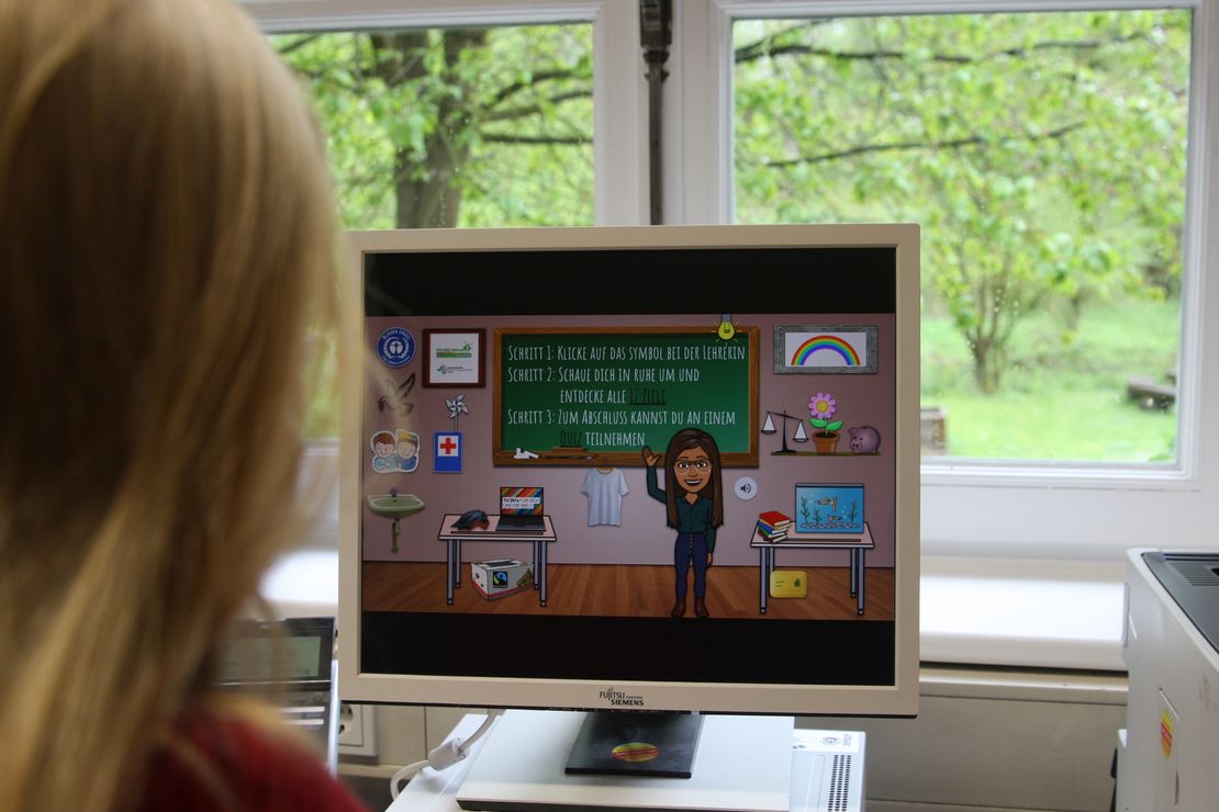 Ein junger Mensch, von hinten zu sehen, sitzt vor einem Computer, der ein interaktives Spiel zeigt.