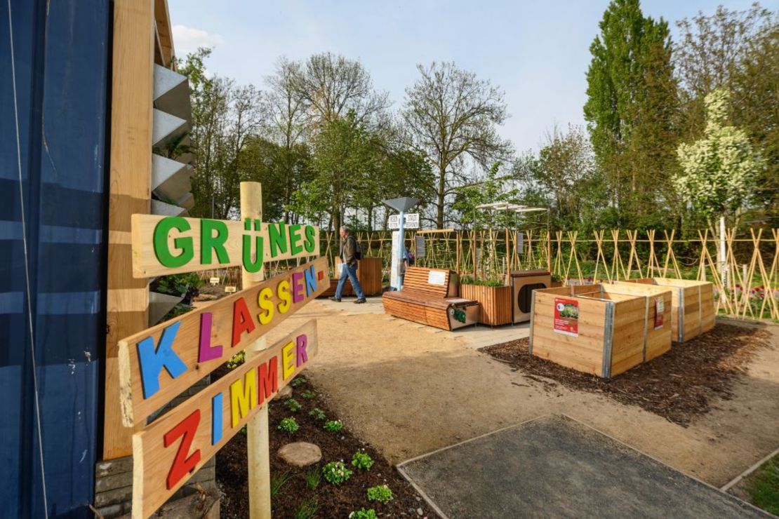 Holzschild mit der Aufschrift "Grünes Klassenzimmer", da hinter sind Hochbeete und Sitzgelegenheiten zu sehen