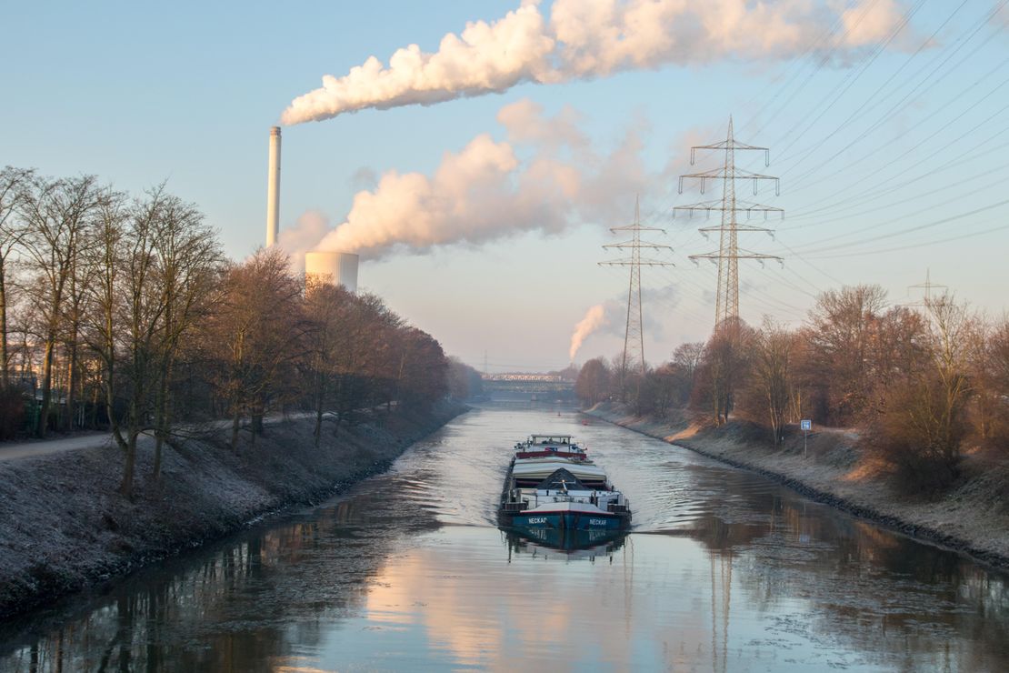 Ein Schiff fährt auf dem Rhein Herne Kanal und im Hintergrund rauchen zwei Industireschornsteine