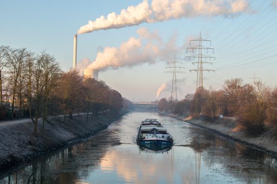 Ein Schiff fährt auf dem Rhein Herne Kanal und im Hintergrund rauchen zwei Industireschornsteine