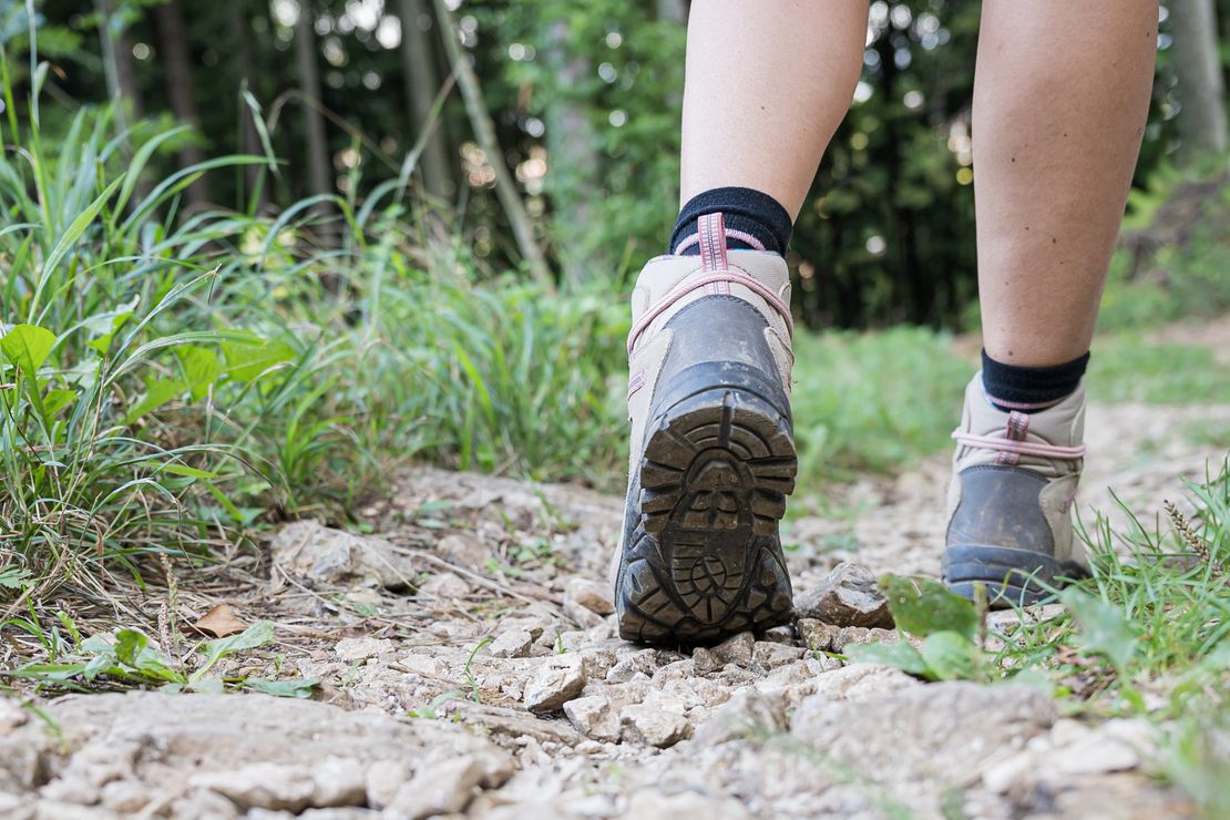 Ein Weg im Grünen aus der Froschperspektive, auf dem ein Mensch in Wanderschuhen schreitet
