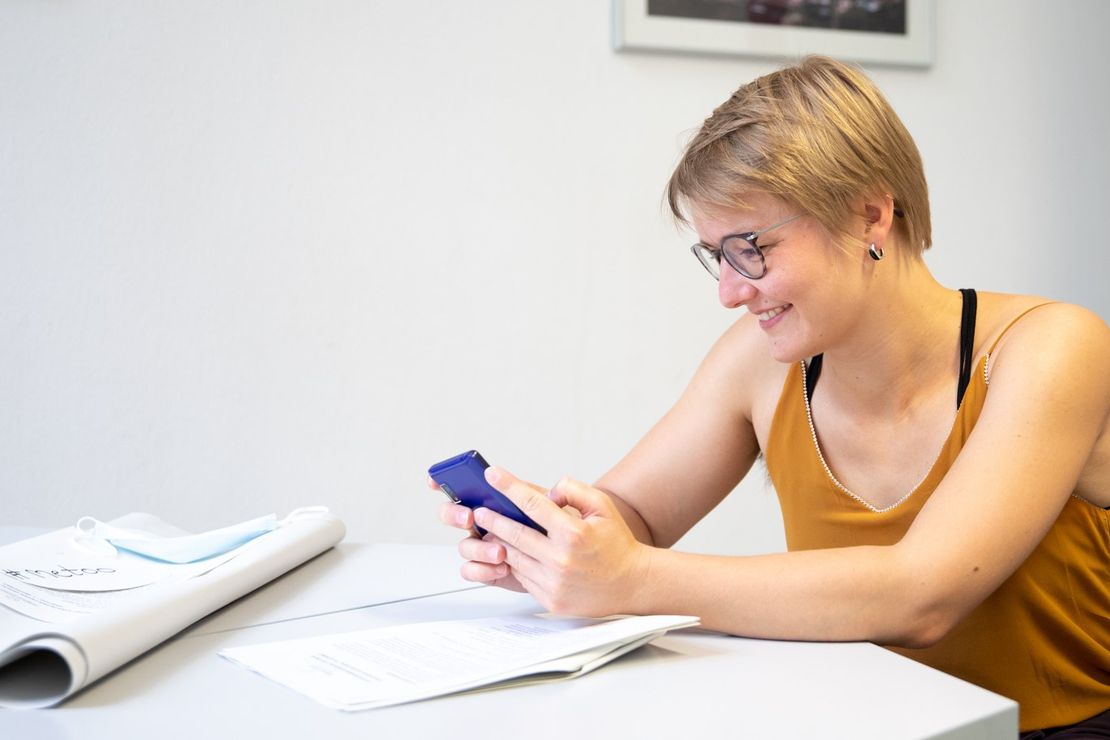 Frau sitzt in einem Seminarraum und guckt sich etwas auf einem Fairphone an