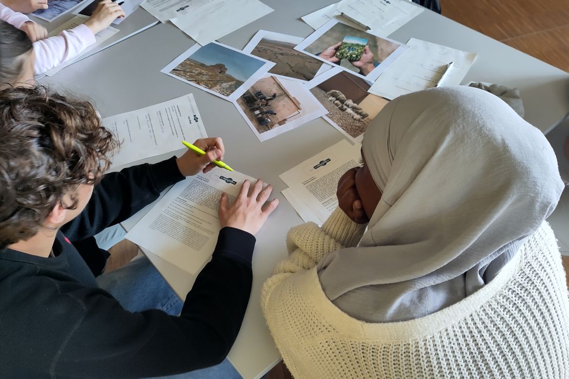 Auf einem Tisch liegen verschidene Bilder und Arbeitsblätter und mehrere Menschen sitzen um den Tisch herum.