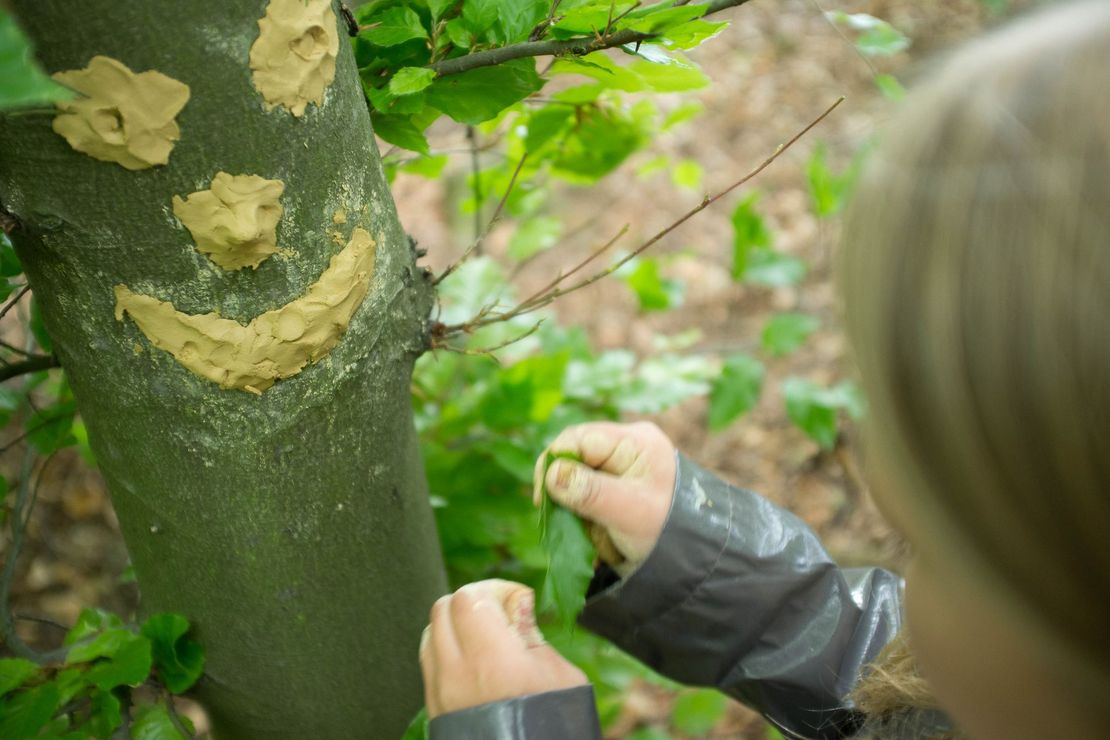 Kind macht ein Gesicht aus Ton an einen Baum