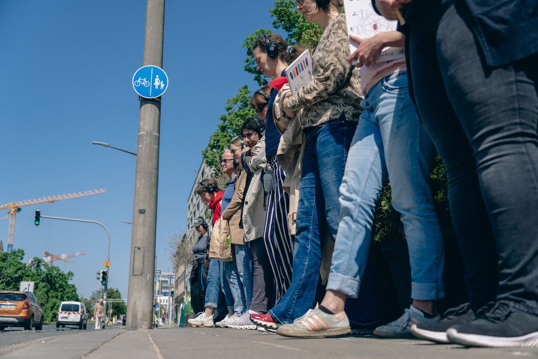 Eine Gruppe von Menschen mit Kopfhören steht in einer Reihe neben einer Strasse