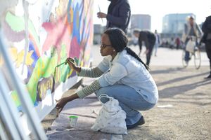 Eine Frau zeichnet ein buntes Bild an eine Steinmauer im öffentlichen Raum.