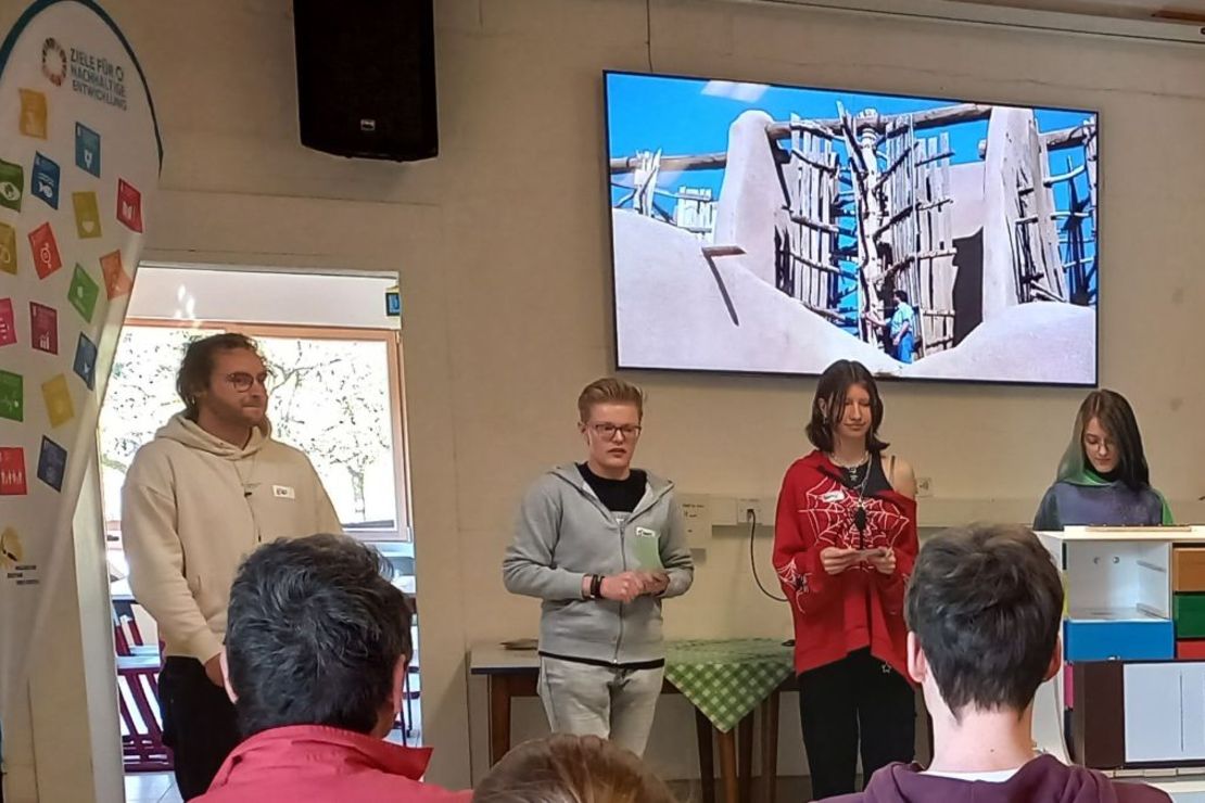 Schüler*innen stehen auf einer Bühne und präsentieren ihr Projekt einem Publikum