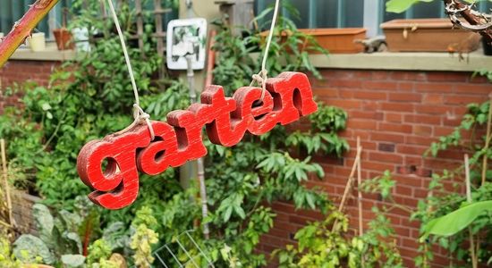 Ein hölzerner Schriftzug "Garten" hängt in einem Garten.
