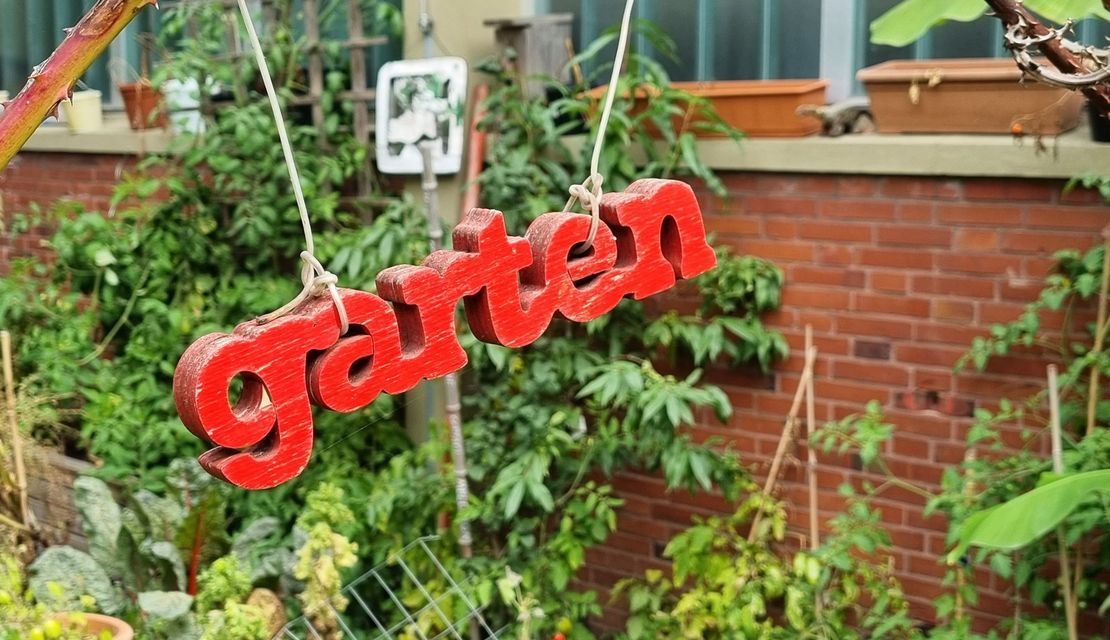 Ein hölzerner Schriftzug "Garten" hängt in einem Garten.