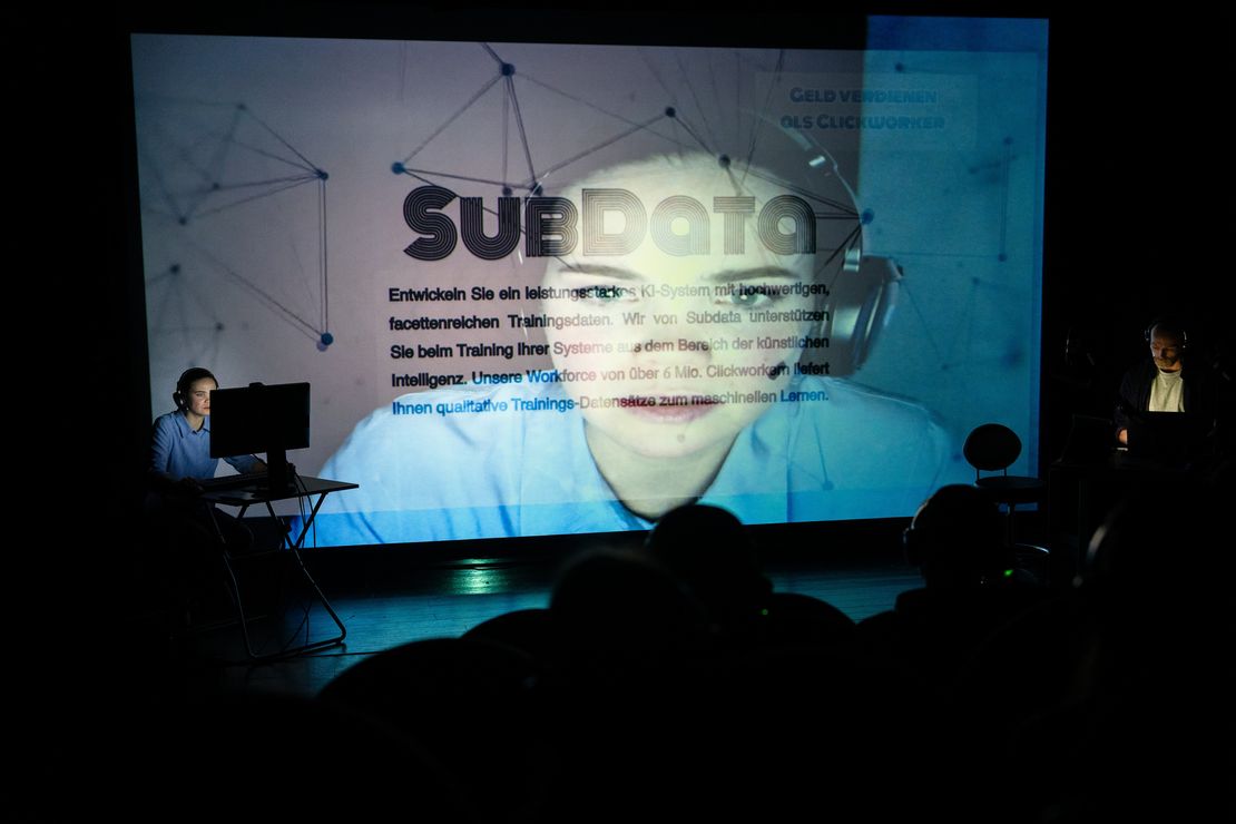 Eine Darstellerin auf der Bühne vor einem Computer, Ihr bild wird auf eine große Leinwand übertragen