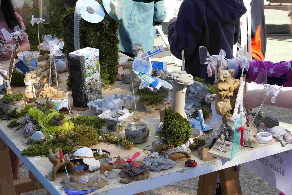 Zu sehen ist eine selbst gebaute Stadt, die aus Naturmaterialien (Ton, Moos u.a.) und upgecycelten Materialien (Tetrapack, CDs u.a.) besteht.