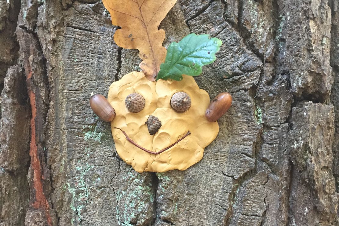 ein mit Ton und Naturmaterialien gestaltetes Lachgesicht an einem Baumstamm