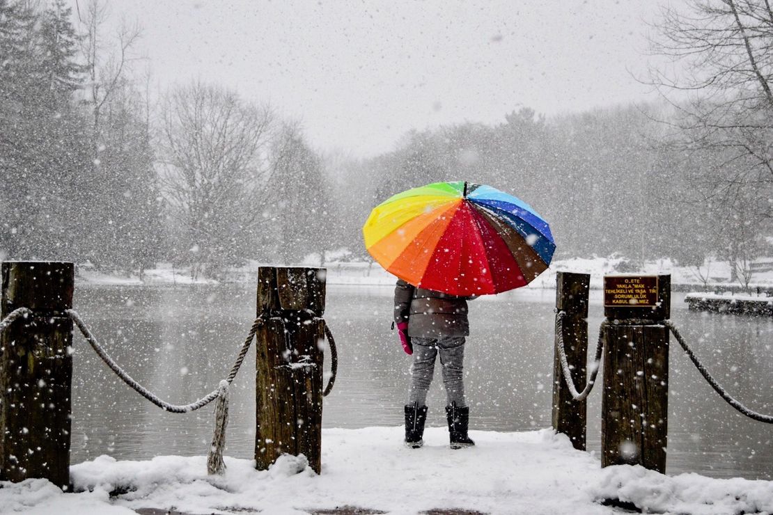 Ein Mench schützt sich vor Schneeflocken mit einem bunten Regenschirm.