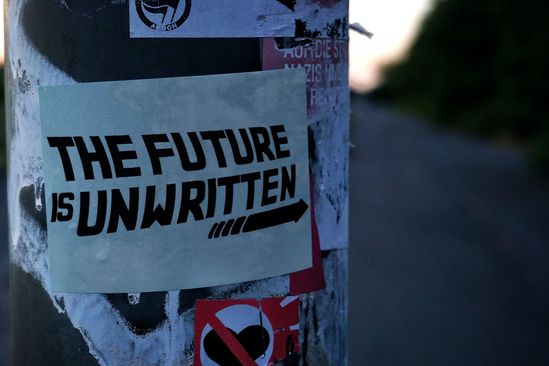 Auf einem Laternenmast ist ein Schriftzug "The future is unwritten" geklebt.