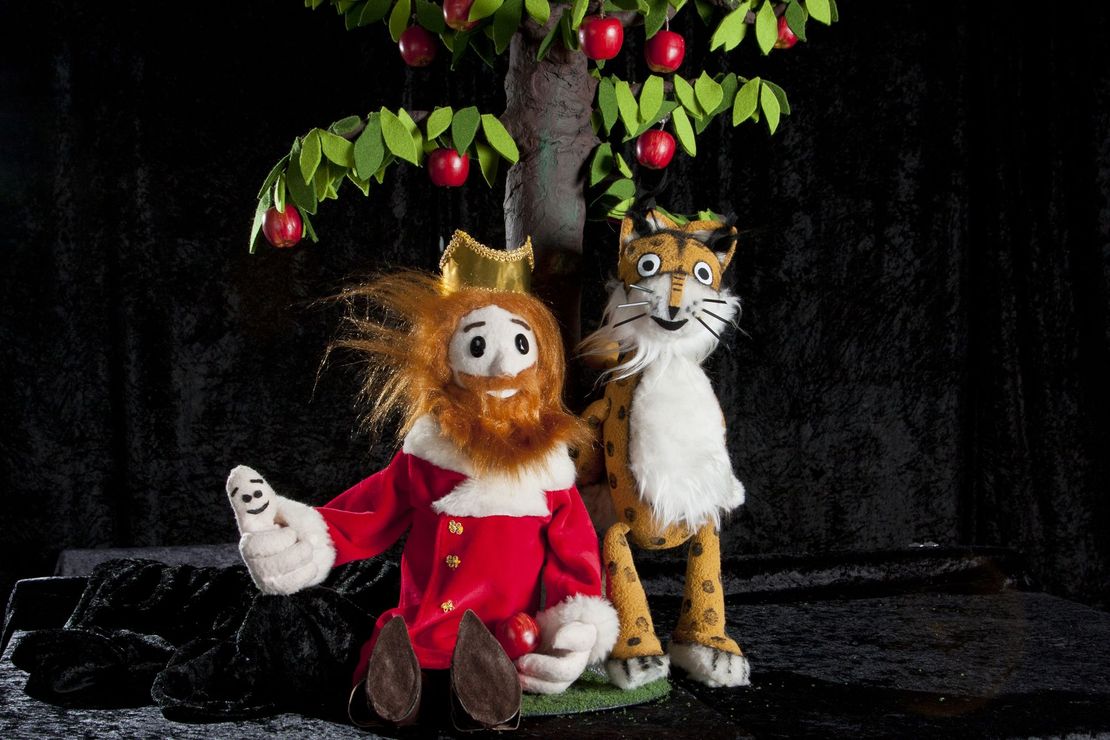 Zwei Figuren aus einem Puppentheater sitzen unter einem Apfelbaum. Es ist der König mit seinem Daumen und ein Luchs.Puppen sizu sehen. Die Hauptdarstelle