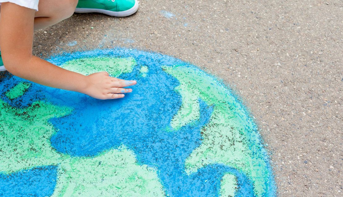 Man sieht eine Weltkugel, die mit Kreide auf den Asphalt gemalt wurde. Ein Kind malt die Weltkugel.