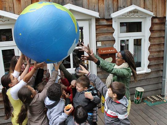 Kinder tragen gemeinsam spielerisch eine Weltkugel auf ihren Händen