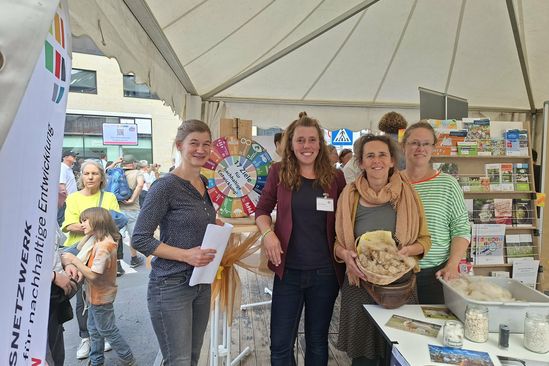 Vier Mitarbeitende der BNE-Regionalzentren stehen in ihrem Infostand und schauen in die Kamera