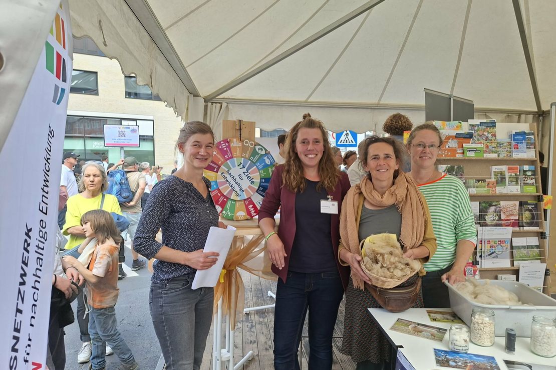 Vier Mitarbeitende der BNE-Regionalzentren stehen in ihrem Infostand und schauen in die Kamera